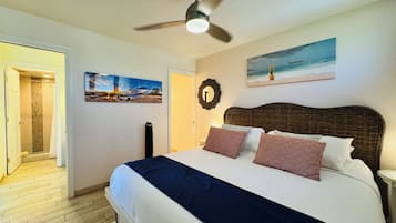 Une chambre à coucher comprenant un lit, un ventilateur de plafond, un tableau et une porte donnant sur une salle de bain.