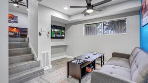 Una sala de estar moderna con un sofá gris, una mesa de centro, un televisor montado en la pared y un ventilador de techo.