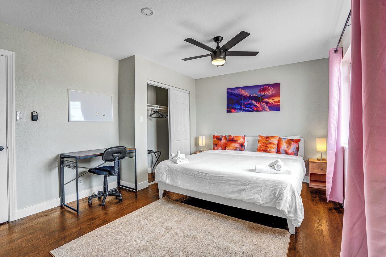 Ein Schlafzimmer mit Bett, Schreibtisch, Stuhl, Deckenventilator und Kunstwerk an der Wand.
