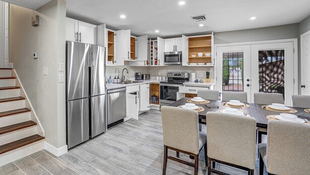 Una cocina moderna con electrodomésticos integrados, un comedor con una mesa lista para cuatro personas, y una escalera que sube a otro nivel.