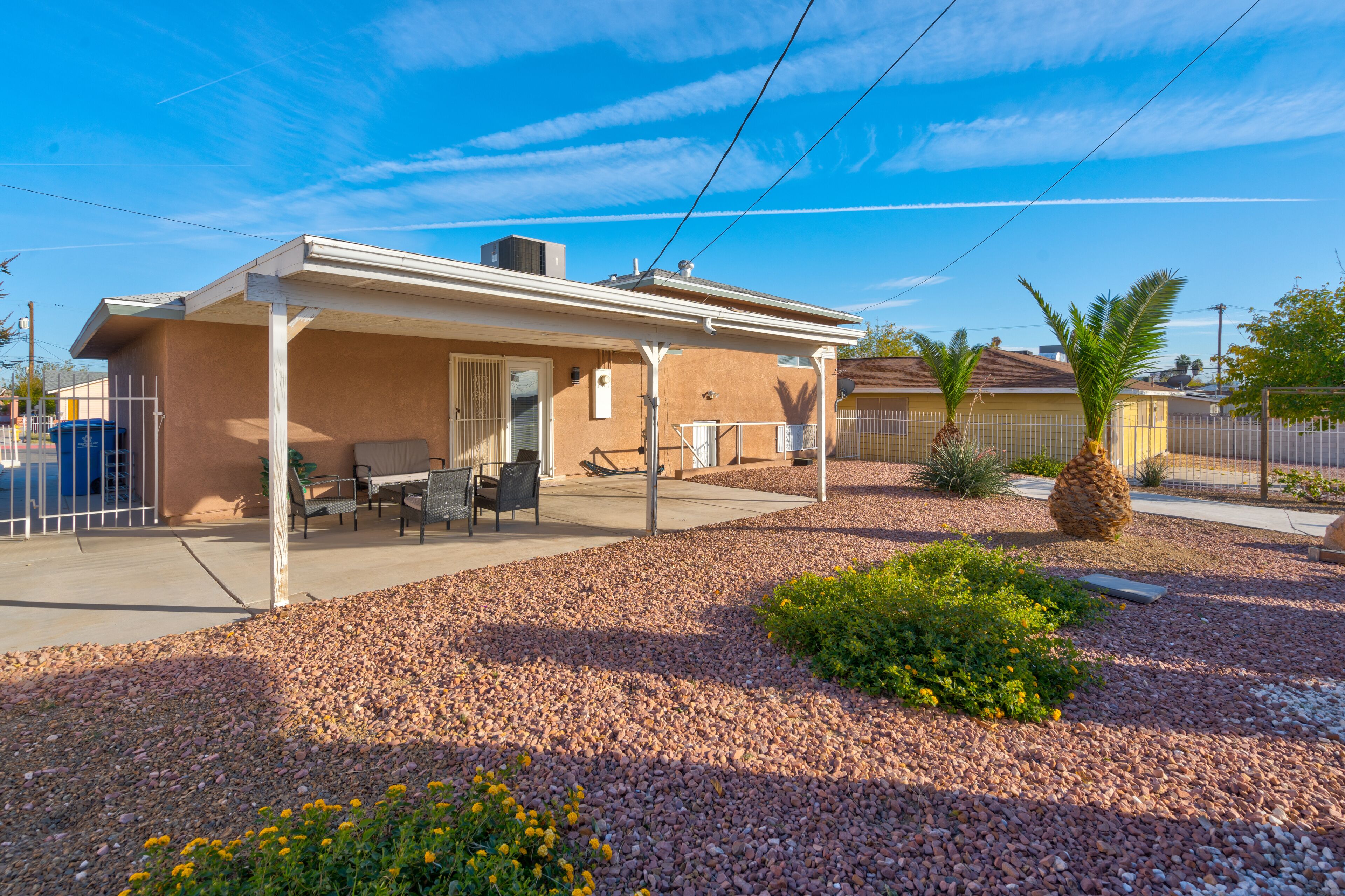 Une maison de plain-pied avec un patio couvert, un petit jardin et un ciel d’un bleu éclatant.