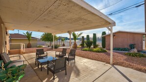 Un patio techado con mobiliario exterior, piso de concreto y vista del barrio circundante.