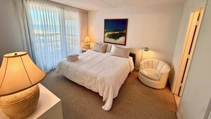 Una habitació d'hotel amb un llit, una cadira, una làmpada, un quadre i vistes per la finestra.