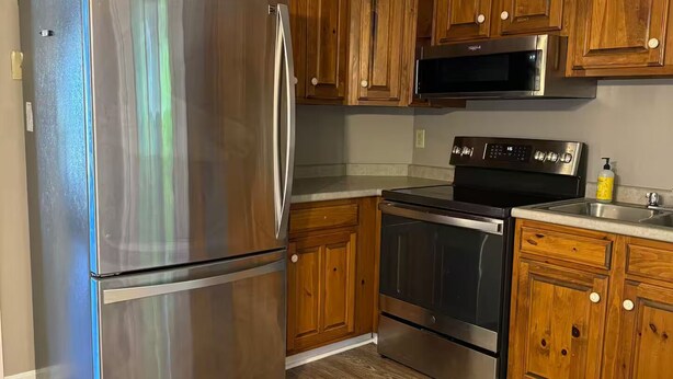 A kitchen with wooden cabinets, stainless steel appliances, and a wooden floor. - Nestled in the trees. (Saco)