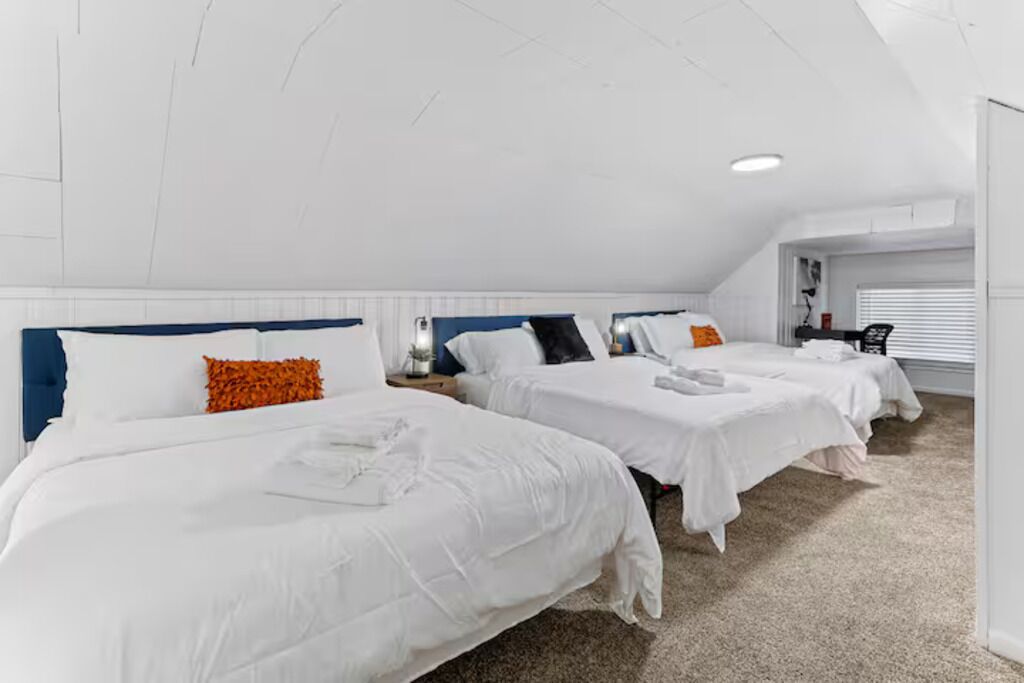 A hotel room with three beds, white bedding, and a ceiling with exposed beams.