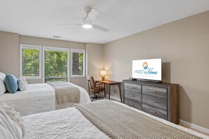 Ein Schlafzimmer mit zwei Betten, einem Schreibtisch, einem Stuhl, einem Fernseher und einem Deckenventilator.