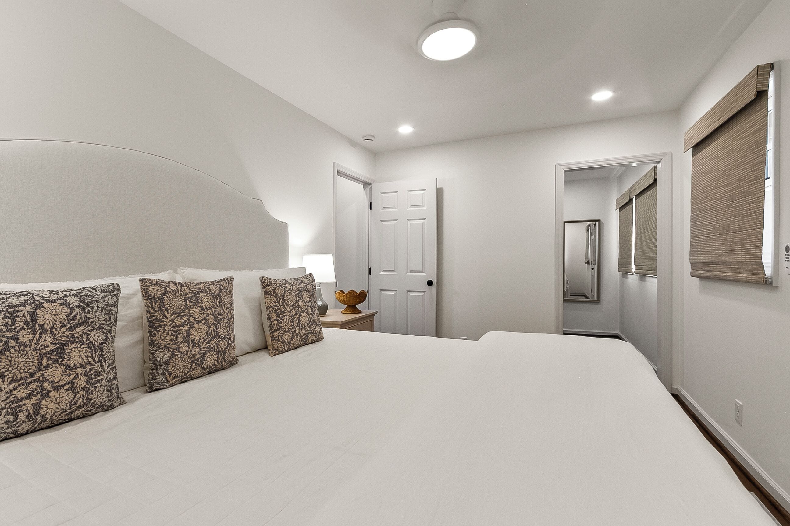 A bedroom with a large bed, a bedside table with a lamp, and a door leading to another room.