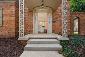 A brick building with a white door and steps leading to a porch with decorative ironwork. - Fully Renovated 4 Bed/3 Bath Home - Walk to Stadium & Downtown (Tuscaloosa)