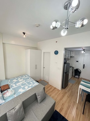 A compact bedroom with a bed, a grey sofa, a kitchenette, and a ceiling fan. - Enjoy a cozy and minimalist unit in the heart of Southwoods, Biñan. (Binan)