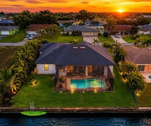 A residential property with a swimming pool, surrounded by a well-maintained lawn and palm trees. - NEW! Canal Escape, Pool, Kayaks & Outdoor Kitchen (Cape Coral)
