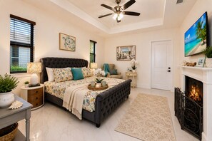 A bedroom with a large bed, a ceiling fan, a fireplace, and a television on the wall. - NEW! Canal Escape, Pool, Kayaks & Outdoor Kitchen (Cape Coral)