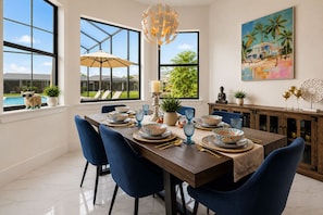 A dining area with a large table set for six, surrounded by blue chairs, with a view of a swimming pool and greenery outside. - NEW! Canal Escape, Pool, Kayaks & Outdoor Kitchen (Cape Coral)