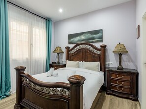 A bedroom with a wooden bed, two bedside tables with lamps, a large window with sheer curtains, and a painting on the wall. - Madrid Centro - 3 bedroom and 2 bathroom apartment with 2 terraces (Ciudad de Madrid)