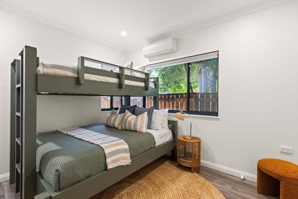 Habitación con literas y vista a la vegetación exterior, una mesita redonda y un aire acondicionado instalado en la pared.