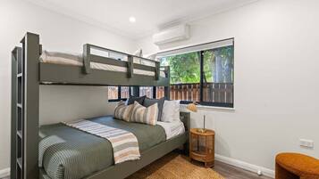Habitación con literas y vista a la vegetación exterior, una mesita redonda y un aire acondicionado instalado en la pared.