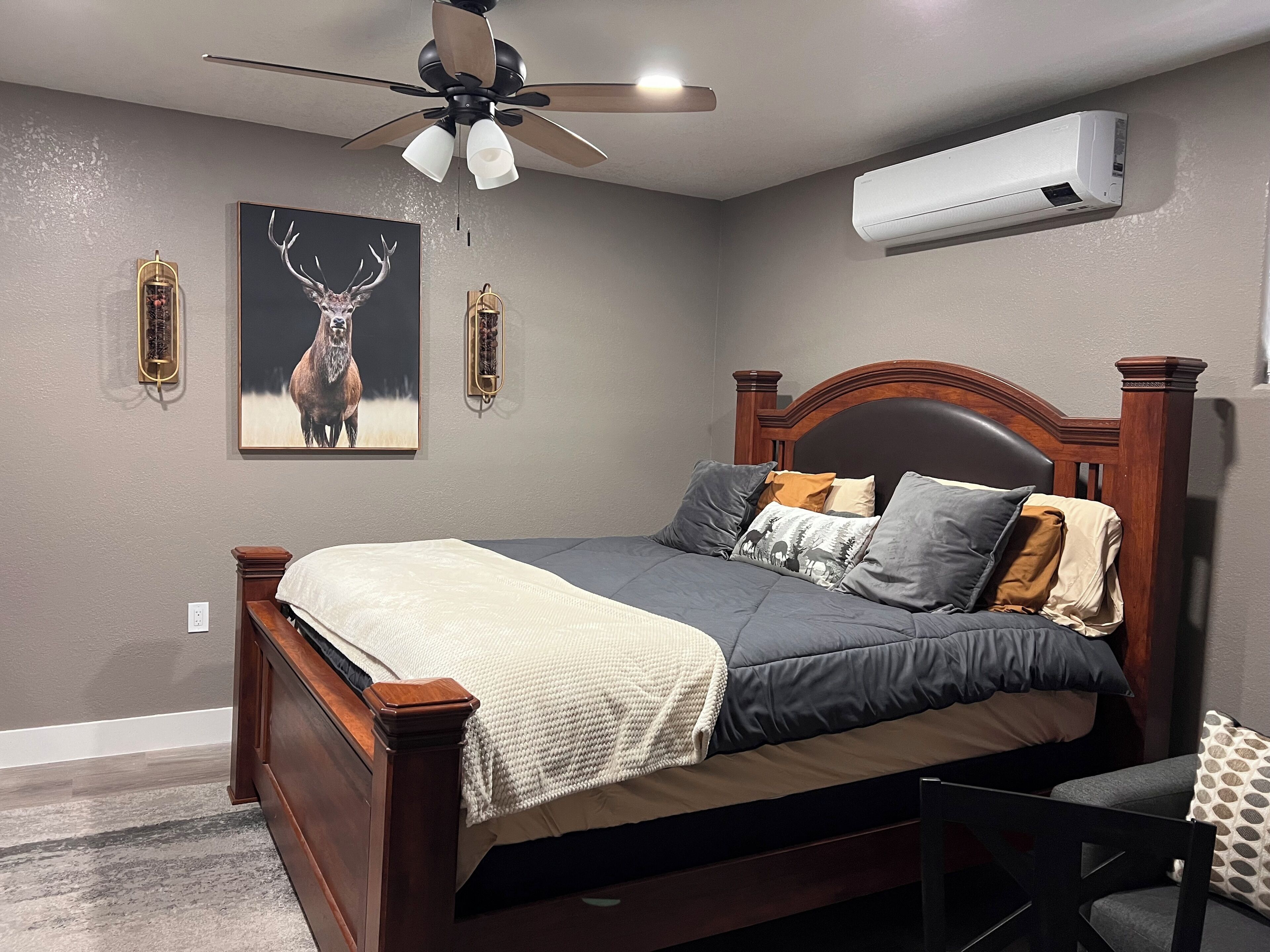 A bedroom with a wooden bed, a ceiling fan, an air conditioner, and a deer painting on the wall.