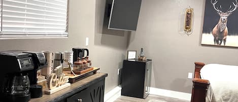 A modern bedroom with a bed, a coffee station, a mounted TV, and a deer painting.