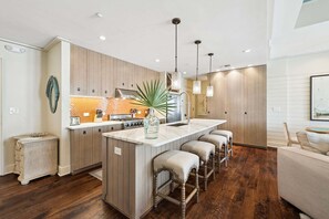 A modern kitchen with a central island, bar stools, pendant lighting, and a wooden floor. - 6 Barrett Place | Elevated Luxury in the Heart of Rosemary Beach (Rosemary Beach)