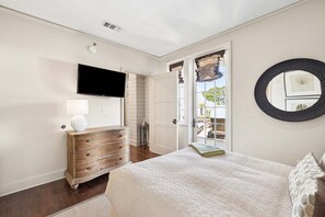 Un dormitorio con cama, cómoda, televisor y puerta que da a un balcón.