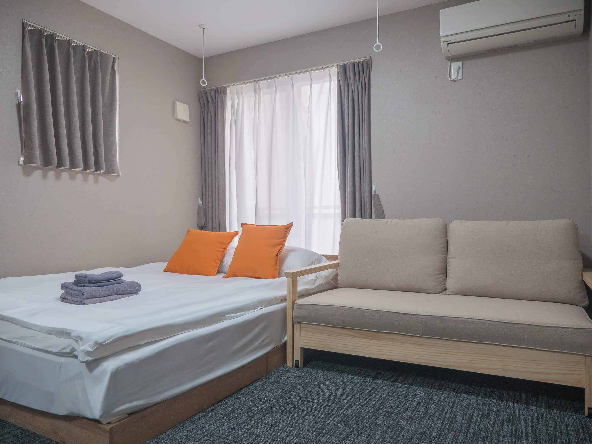 Une chambre d’hôtel comprenant un lit, un canapé, une fenêtre avec des rideaux, un appareil de climatisation et un sol recouvert de moquette.