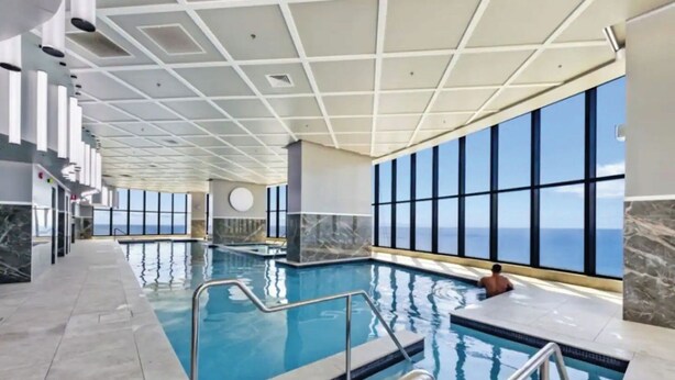 En stor inomhuspool med fantastisk utsikt över havet genom stora fönster, ett kaklat golv och en modern takdesign.