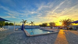 Ein Swimmingpool mit Liegestühlen, Palmen und einem Sonnenuntergang im Hintergrund.