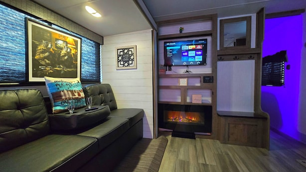 Ein gemütliches Wohnzimmer mit Ledersofa, Kamin, Wandfernseher und gerahmten Kunstwerken an der Wand.