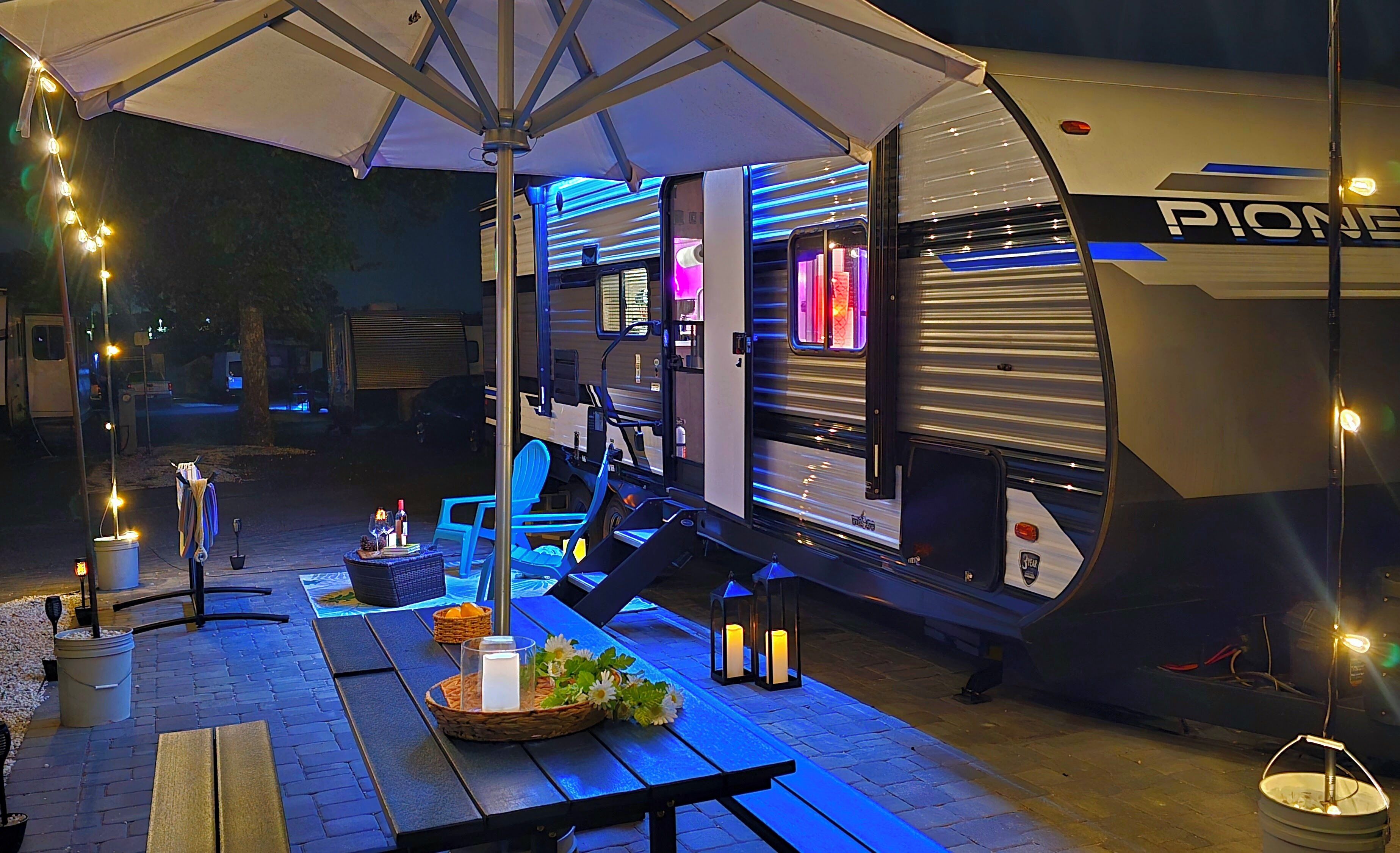 Un camper fermo con una zona esterna coperta, un tavolo da picnic e luci decorative appese.