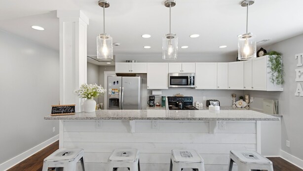 Una cocina moderna con armarios blancos, electrodomésticos de acero inoxidable e iluminación colgante.