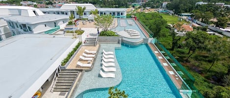 A rooftop swimming pool with lounge chairs, a view of the surrounding landscape, and a building with a white facade.