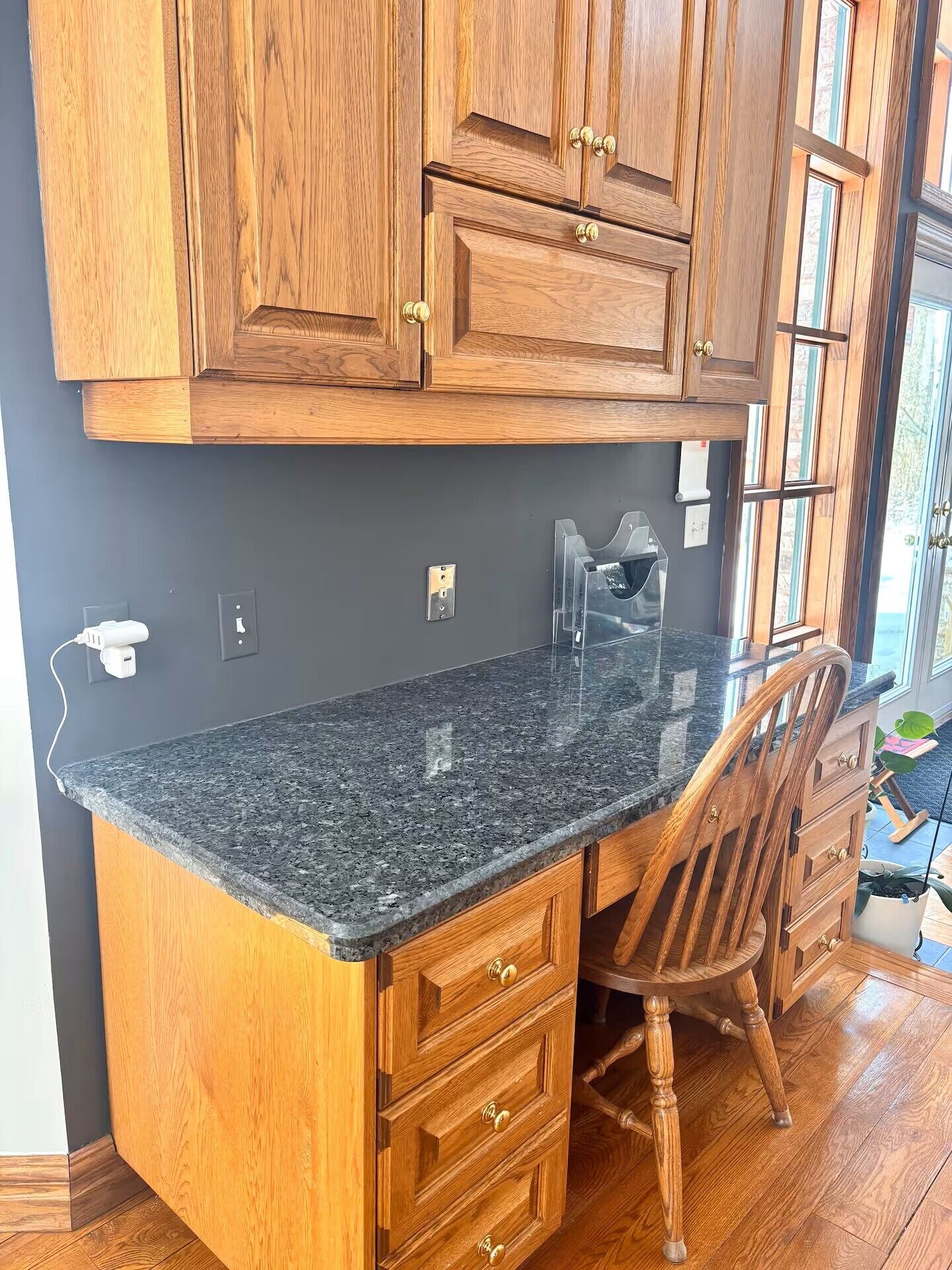 A kitchen with wooden cabinets, a granite countertop, a chair, and a potted plant.