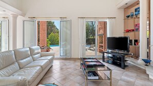 A spacious living room with a white leather sofa, a glass coffee table, and a flat-screen TV. - Villa Harmonie - Welkeys (Villeneuve-Loubet)