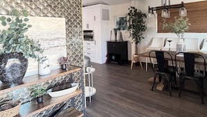 Una cocina moderna con suelo de madera oscura, armarios blancos y una zona de comedor con mesa y sillas de madera.
