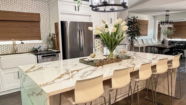 Una cocina moderna con una isla de mármol, electrodomésticos de acero inoxidable y un comedor con taburetes de bar.