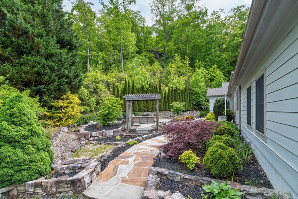 A stone pathway leading to a wooden gazebo surrounded by lush greenery and a variety of shrubs.
