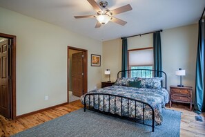 Ein Schlafzimmer mit Bett, Deckenventilator, Fenster mit Vorhängen, Nachttisch und einer Tür.