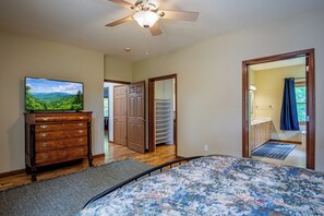 Ein Schlafzimmer mit Bett, Kommode, Deckenventilator, Fernseher und Blick auf einen Kleiderschrank und ein Badezimmer.