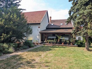 A two-story house with a tiled roof, a covered porch with potted plants, and a well-maintained garden. - Holiday flat on the upper floor with Wi-Fi and air conditioning (Zamárdi)