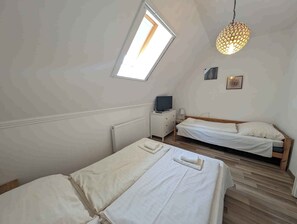 A bedroom with two beds, a television, a radiator, a window, and a hanging light fixture. - Holiday flat on the upper floor with Wi-Fi and air conditioning (Zamárdi)