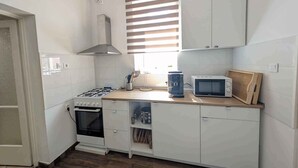 Una cuina compacta amb armaris blancs, fog ó a gas, microones i forn integrat.