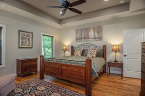 A bedroom with a wooden bed, two bedside tables with lamps, a ceiling fan, a window with blinds, and a door. - 3BR Retreat in Connestee Falls with Fireplace, Community Pool, and Garage (Brevard)