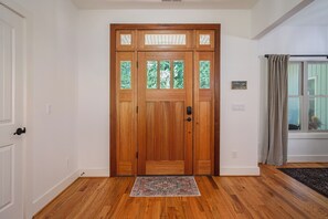 A wooden front door with glass panels, a doormat, and a window with curtains. - 3BR Retreat in Connestee Falls with Fireplace, Community Pool, and Garage (Brevard)