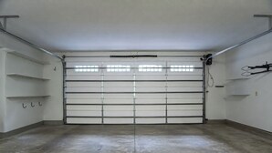 A garage with a closed garage door, concrete floor, and metal shelving units on the walls. - 3BR Retreat in Connestee Falls with Fireplace, Community Pool, and Garage (Brevard)