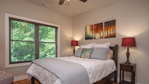 A bedroom with a large window, a bed with patterned bedding, two wall-mounted lamps, and two paintings. - 3BR Retreat in Connestee Falls with Fireplace, Community Pool, and Garage (Brevard)