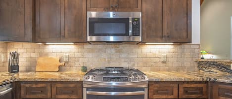Una cocina con armarios de madera, un microondas de acero inoxidable, una estufa a gas y un horno empotrado.