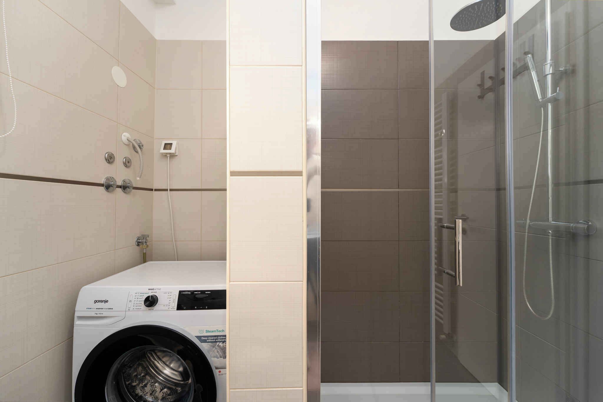 Une salle de bain équipée d’un lave-linge, d’une douche à parois de verre et de toilettes.