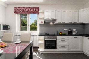 A modern kitchen with white cabinets, a black countertop, and a window with a red valance. - Holiday apartment near Pical Beach (Poreč)