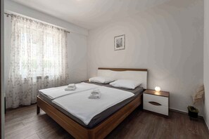 A bedroom with a wooden bed, white bedding, a nightstand with a lamp, and a window with sheer curtains. - Holiday apartment near Pical Beach (Poreč)