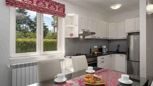 A modern kitchen with white cabinets, a stainless steel refrigerator, and a dining table set with white cups and a croissant tray. - Holiday apartment near Pical Beach (Poreč)