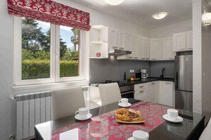 A modern kitchen with white cabinets, a stainless steel refrigerator, and a dining table set with white cups and a croissant tray. - Holiday apartment near Pical Beach (Poreč)